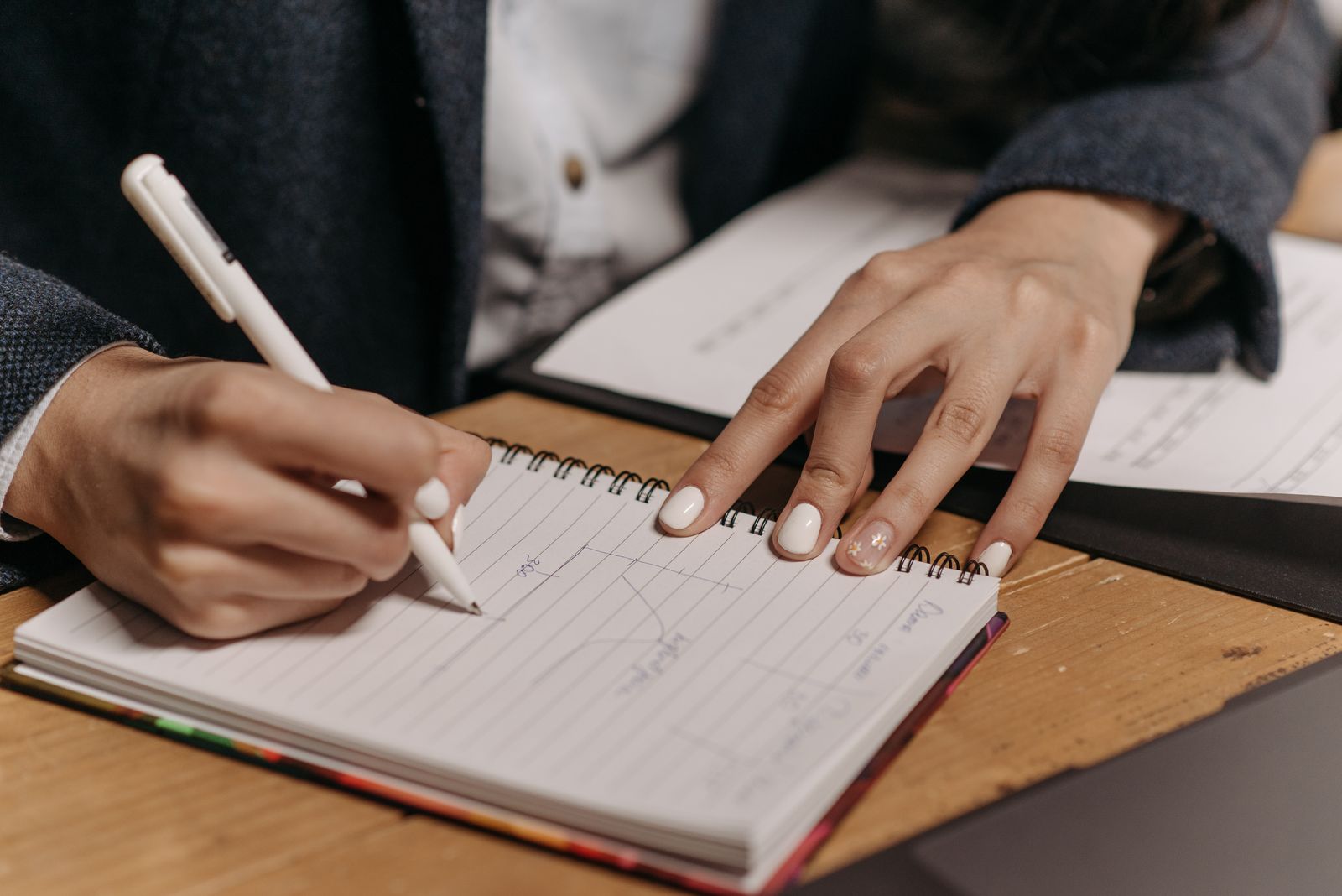 A person writing a personal motivation letter at a desk with a notebook and open laptop