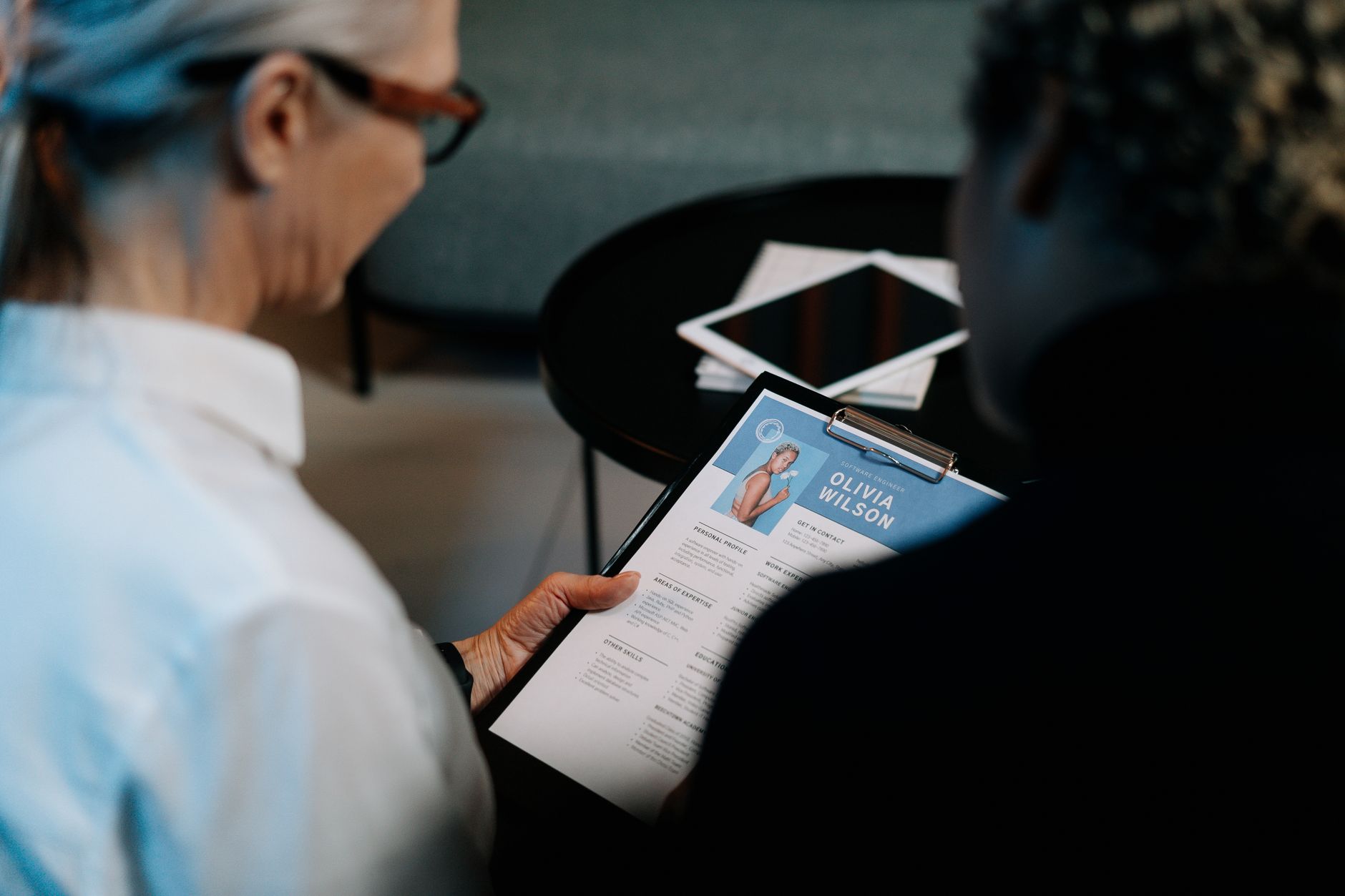A person reviewing a resume draft on a laptop screen at a desk, with a printed resume and coffee cup nearby