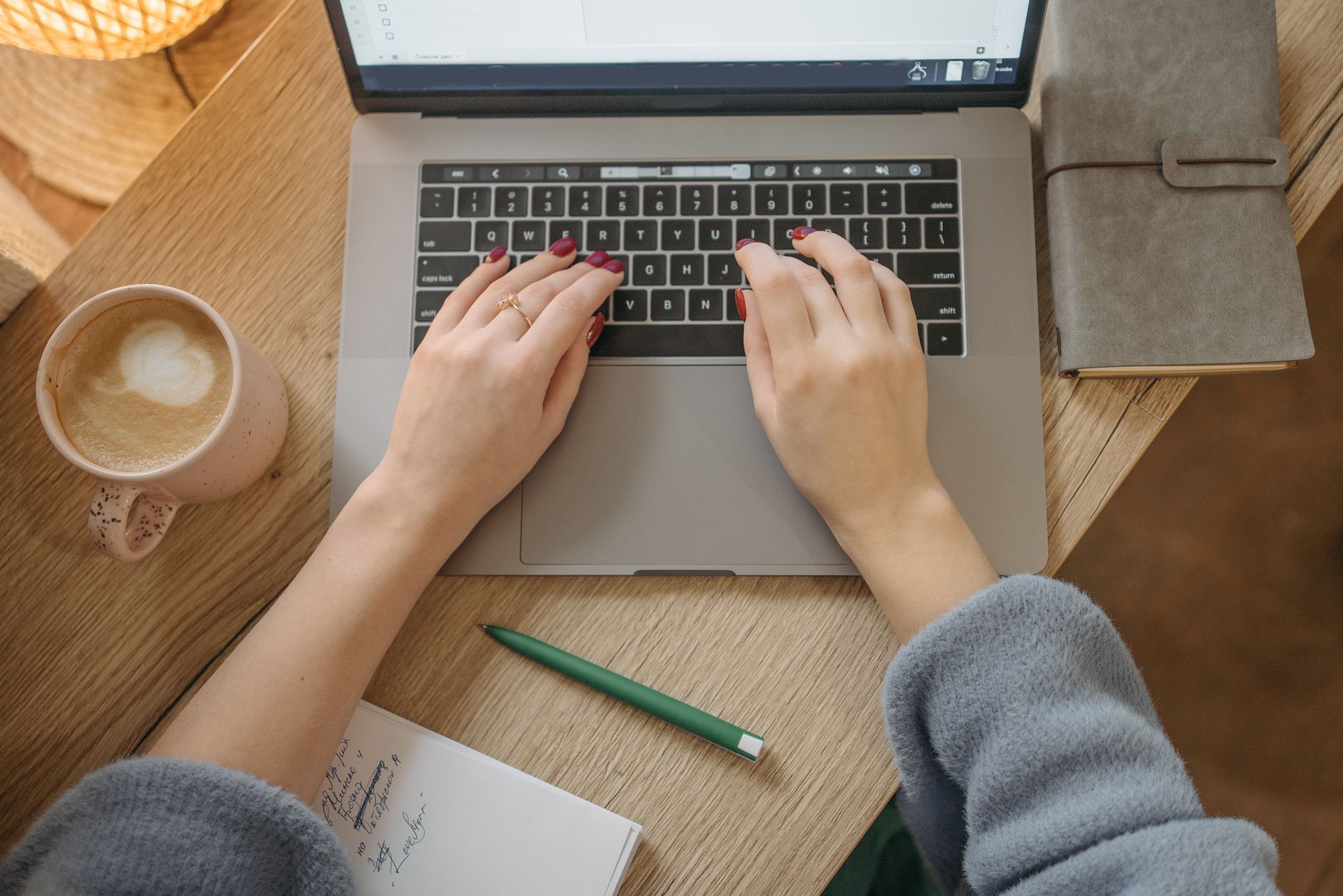 Person typing on a laptop at a desk with a notebook and coffee cup, drafting a cover letter
