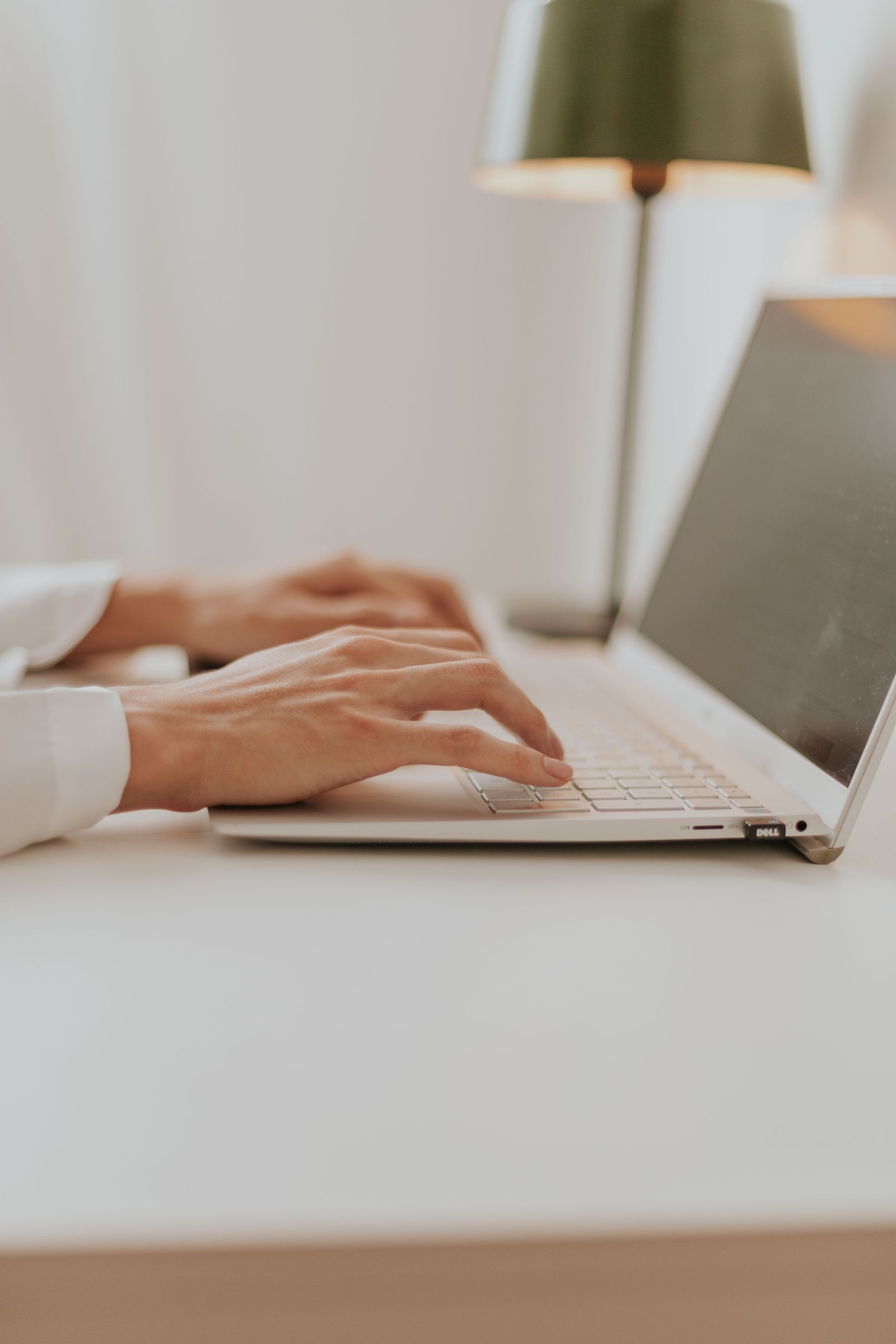Close-up of hands typing on a laptop keyboard next to a notebook with handwritten notes, drafting resume content